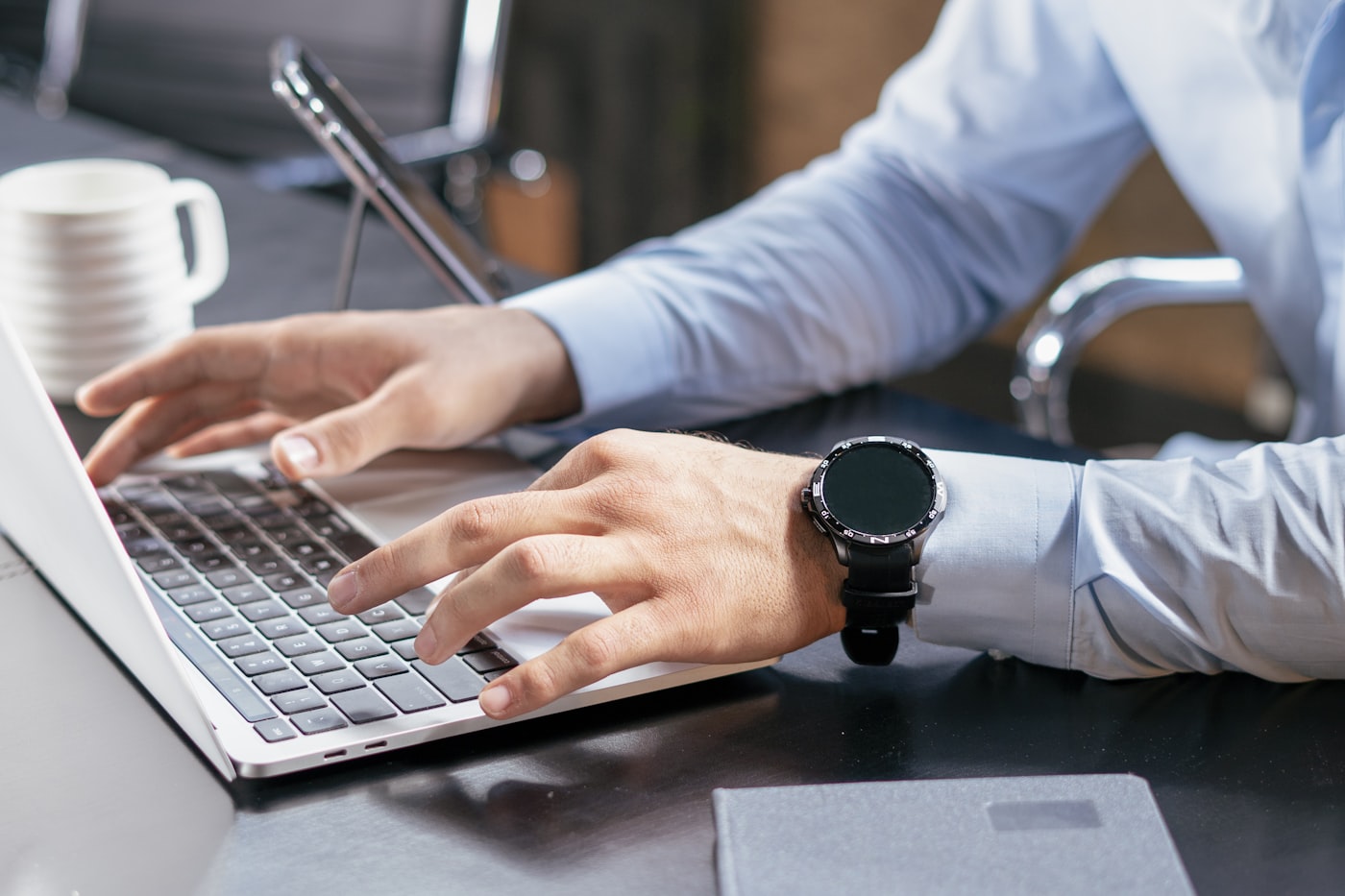 Persona escribiendo en un notebook con reloj inteligente